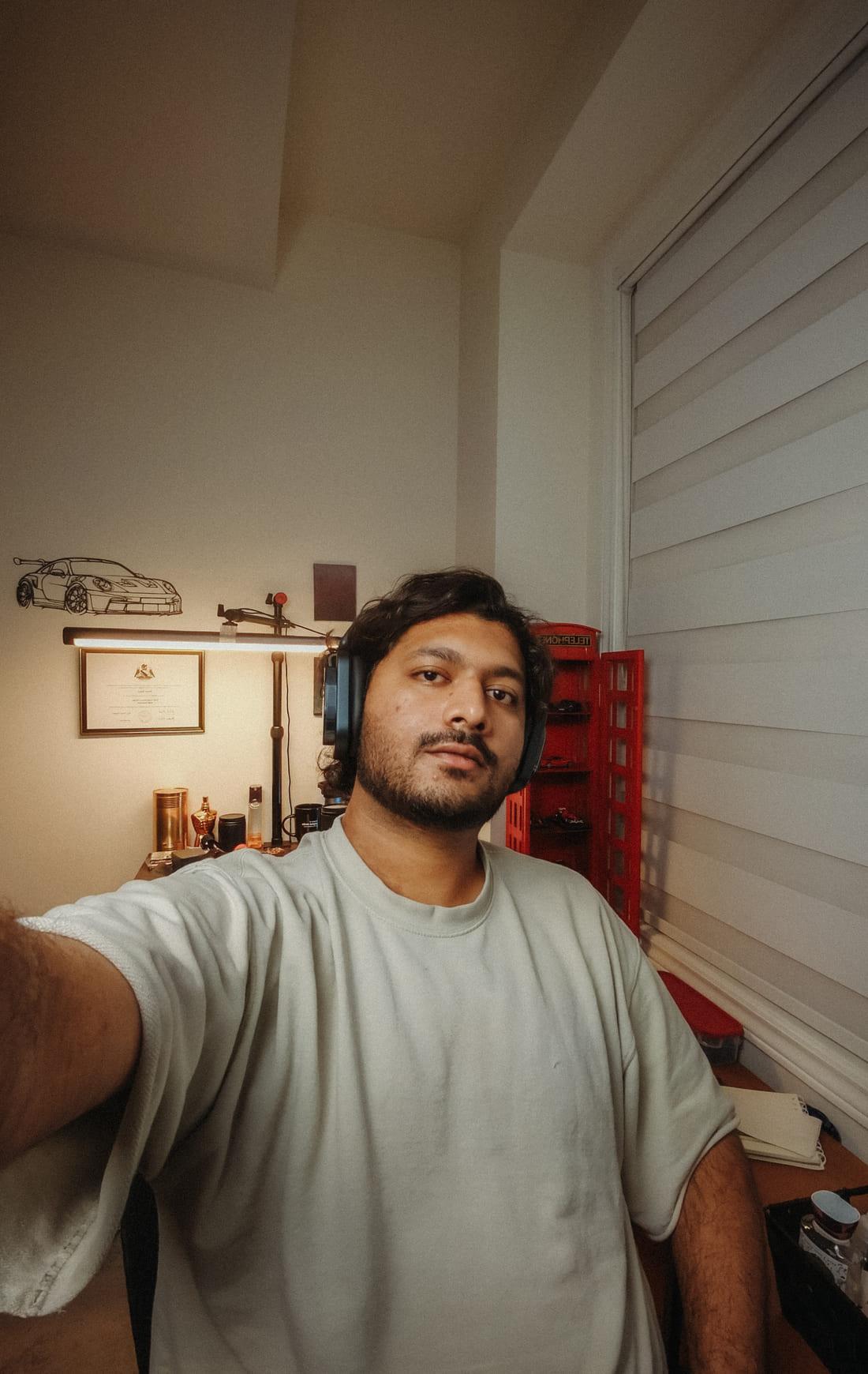 Shrey Patel at home, with a sketched metal outline of a sports car mounted on the wall behind him and a framed certificate below it.